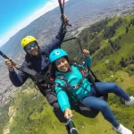 Selfie de dos turistas sonrientes disfrutando de un emocionante vuelo de Parapente en tándem sobre las montañas de Medellín. Representa la aventura aérea y la experiencia inolvidable de alta adrenalina.