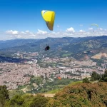 Vuelo de Parapente en San Félix sobre el Valle de Aburrá en un día despejado, con vistas panorámicas de la ciudad de Medellín. Representa la adrenalina y la aventura aérea privada.