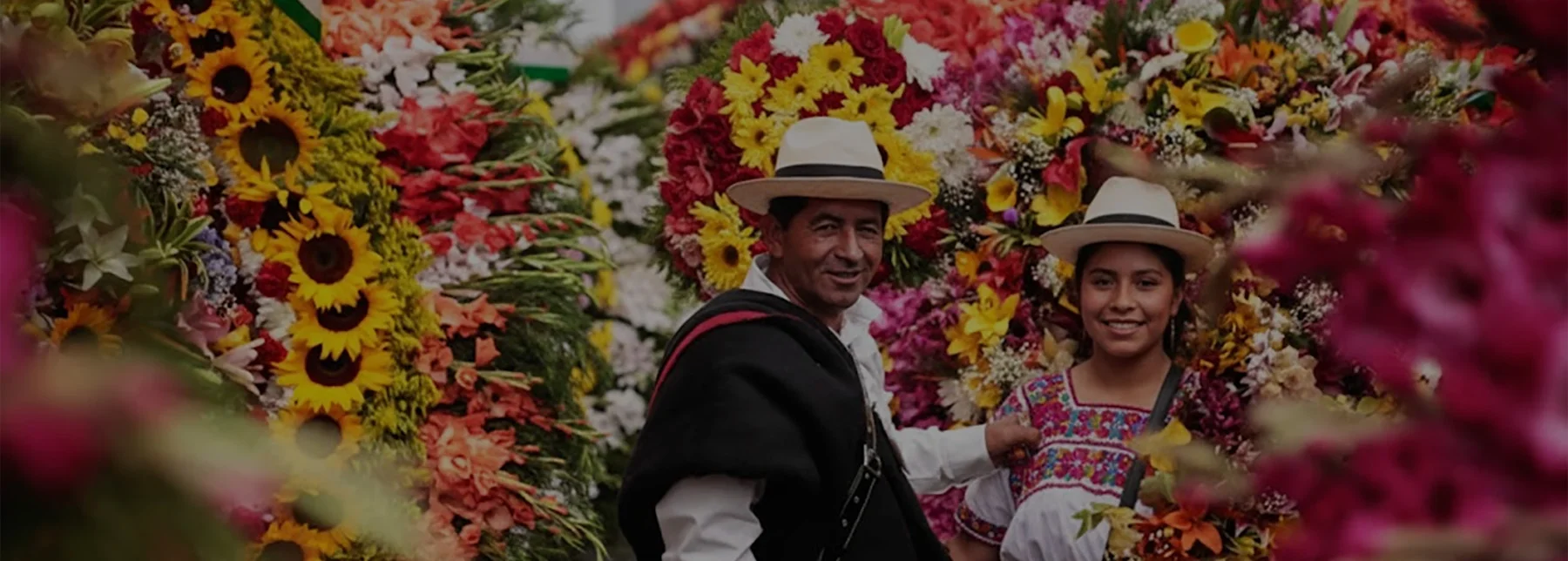 Maestro Silletero y su hija, vestidos con trajes típicos, sonríen en medio de sus silletas florales, representando la herencia y tradición del Tour Silletero en Santa Elena, Medellín.